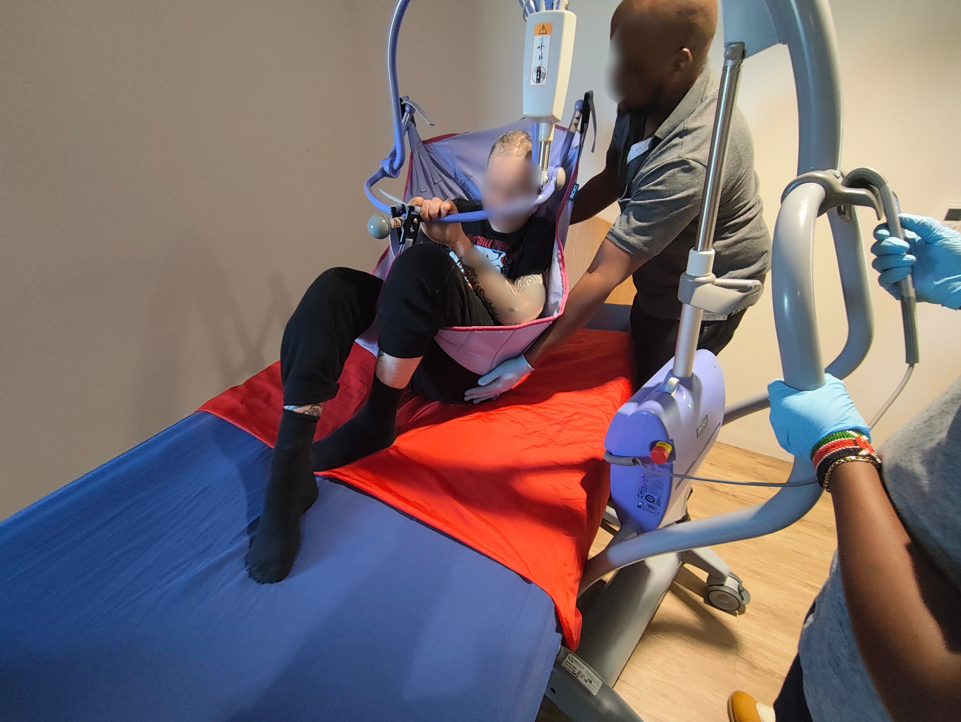 Physiotherapist and support worker assisting a patient with a ceiling hoist transfer