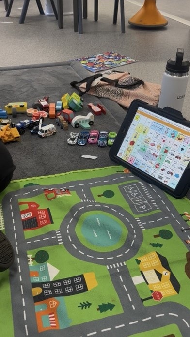 AAC communication device alongside play mat and toy vehicles used in a speech therapy session