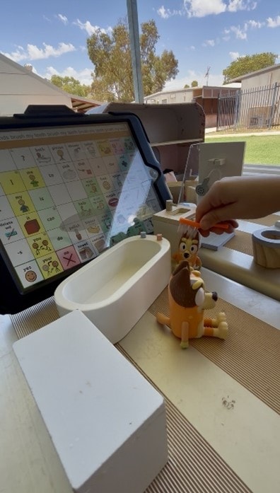Child engaging with AAC communication board and Bluey figurines in an outdoor therapy session
